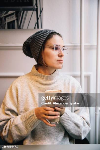 young woman in eyeglasses drinking coffee in a cafe - hipster coffee shop candid stock-fotos und bilder
