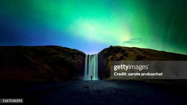 silhouette women and skogafoss waterfall with northern light or aurora borealis  , iceland waterfall travel nature famous tourist destination - noorderlicht sterren stockfoto's en -beelden