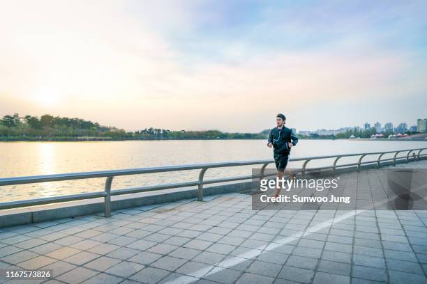 sporty man with earphones jogging at lake park - waterfront stock photos et images de collection