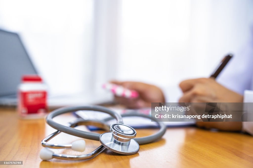 Close-up of doctor's hands writing prescription and holding bottle with pills. Healthcare, medical and pharmacy concept,Drug research, medicine