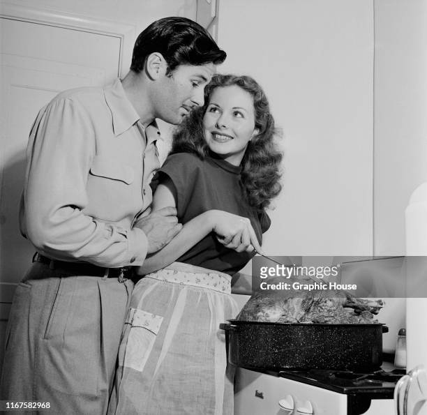 American actress Jeanne Crain and her husband Paul Brinkman cooking a large turkey at home, circa 1955.