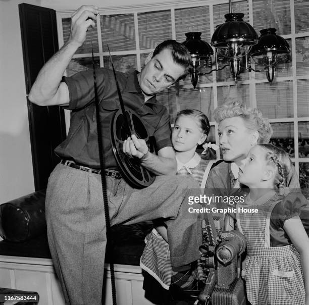 American actress Eve Arden examines some film stock with her husband Brooks West and their two daughters, circa 1960.