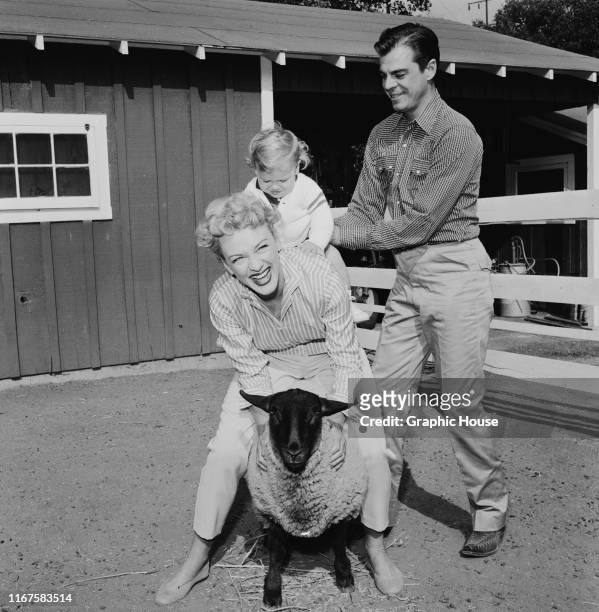 American actress Eve Arden playing with her husband Brooks West, their son Douglas, and a sheep, circa 1960.