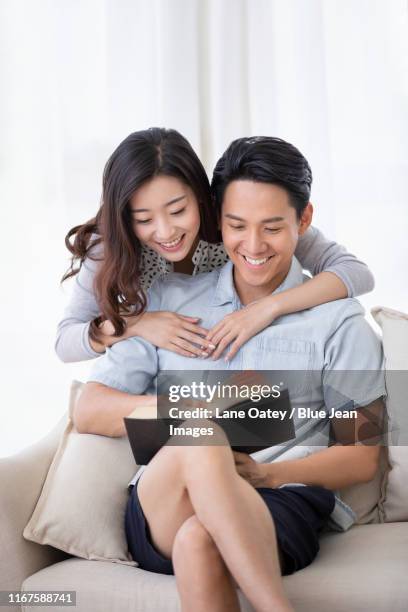 happy young chinese couple reading book in living room - book sleeve stock pictures, royalty-free photos & images