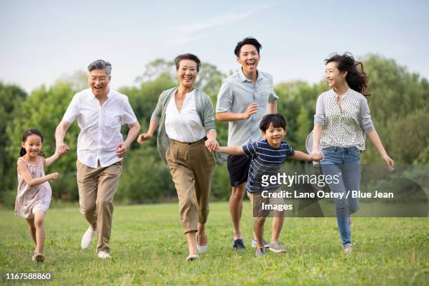happy chinese family running on grass - multi generation family portrait stock pictures, royalty-free photos & images