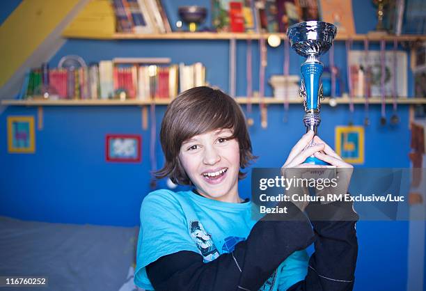 smiling boy holding trophy in bedroom - trophy display stock pictures, royalty-free photos & images