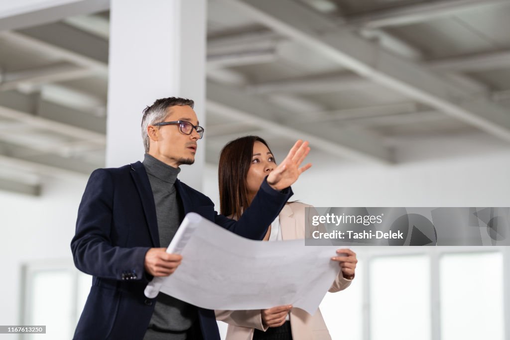 Businesspeople Meeting To Look At Plans In Empty Office