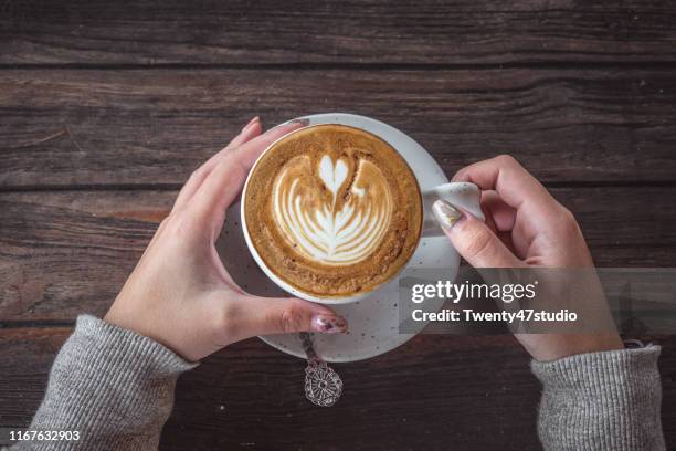 morning hot coffee. closeup of an woman hands having a cup  on wooden table in cafe - hand resting on wood stock-fotos und bilder