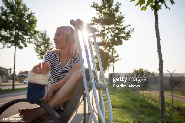 jonge vrouw met gebroken been genieten in een zonnige zomerdag - crutches stockfoto's en -beelden