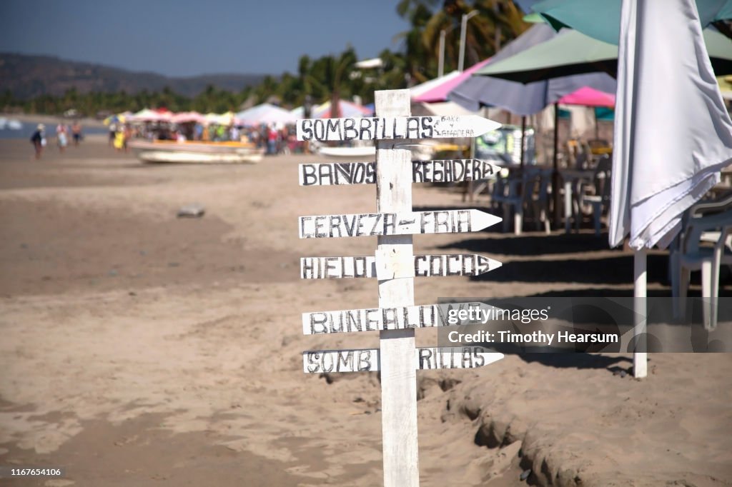 Sign post in Spanish with a sea of umbrellas beyond on a beach on Tenacatita Bay, Costalegre, Jalisco, Mexico