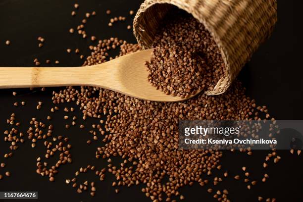 buckwheat seeds in wooden spoon on a brown wooden table - buckwheat fotografías e imágenes de stock