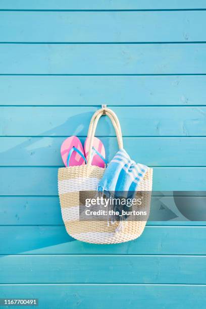 beach bag with towel and flip-flops hanging at a blue painted wooden wall - beach bag stockfoto's en -beelden