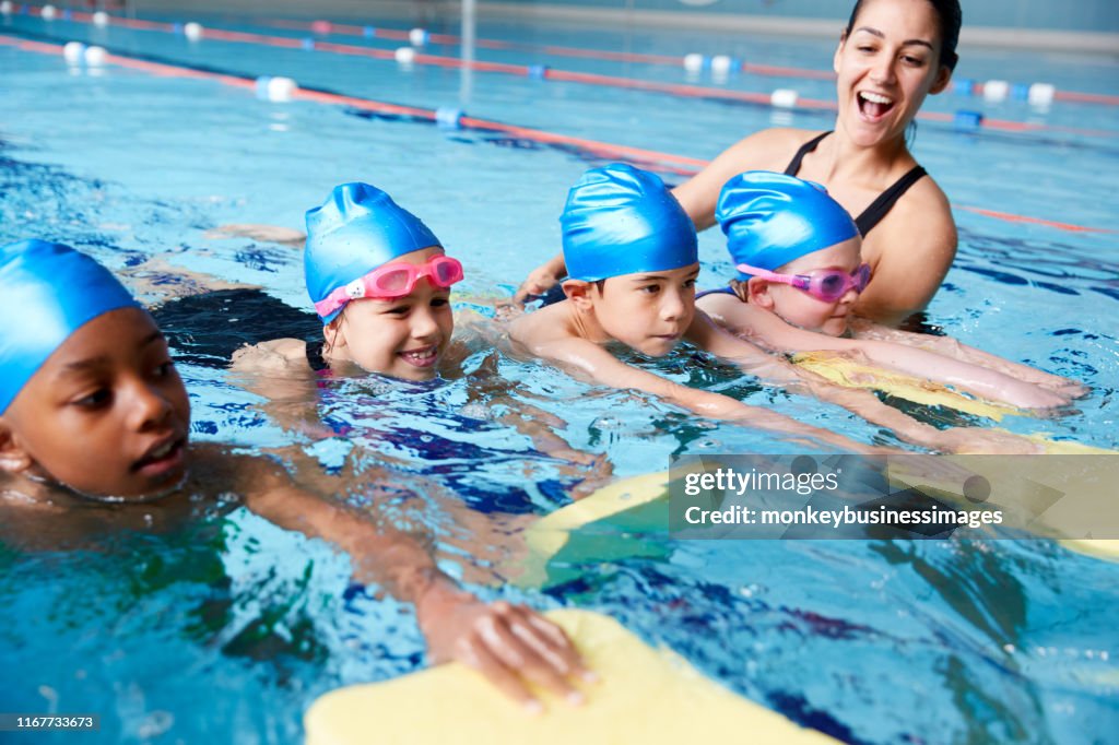 Female Coach In Water Giving Group Of Children Swimming Lesson In Indoor Pool