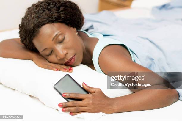 beautiful woman sleeping in bed with her cell phone in her hand - woman 45 sleeping stock pictures, royalty-free photos & images