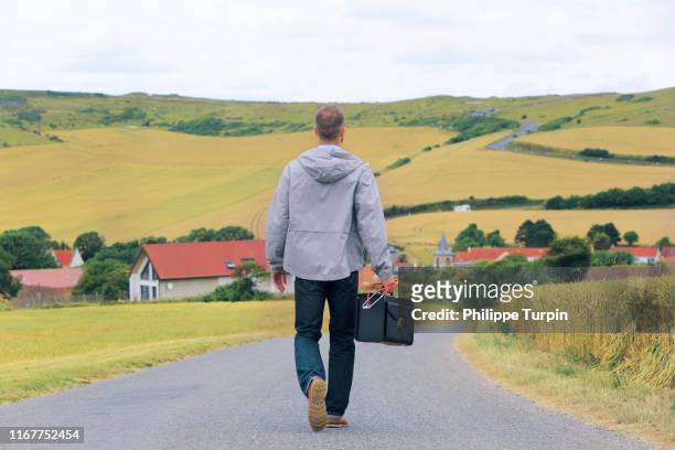 medical deserts, a young doctor back on a country road, a village in the background - campagne photos et images de collection