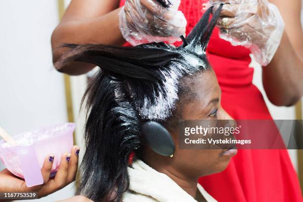 the dresser straightens the hair of this young woman by applying a hair product. - black hair imagens e fotografias de stock