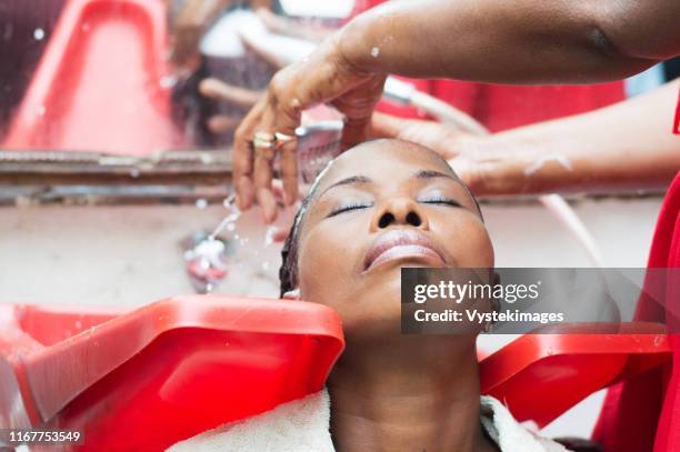 the hairdresser washes the hair of her customer after wiping. - hairdressers black woman stock-fotos und bilder