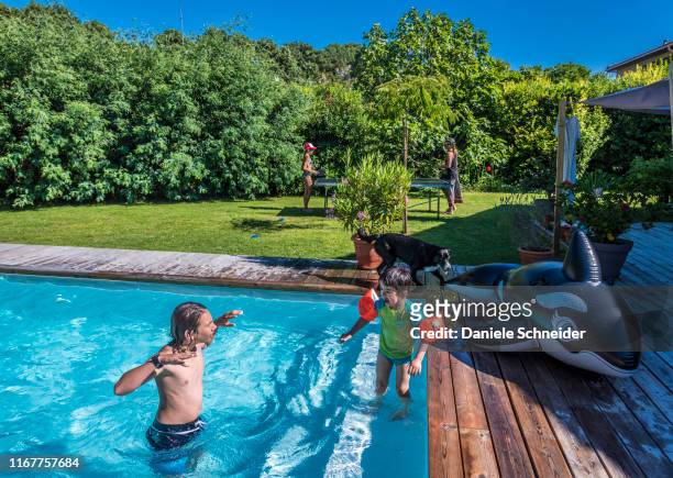 two boys of 5 years old and 13 years old playing in the swimming pool, in the background a mother playing ping pong with her daughter - french garden stock pictures, royalty-free photos & images