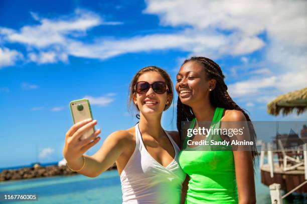 2 smiling girls taking a selfie against blue sky background. - martinique stock pictures, royalty-free photos & images