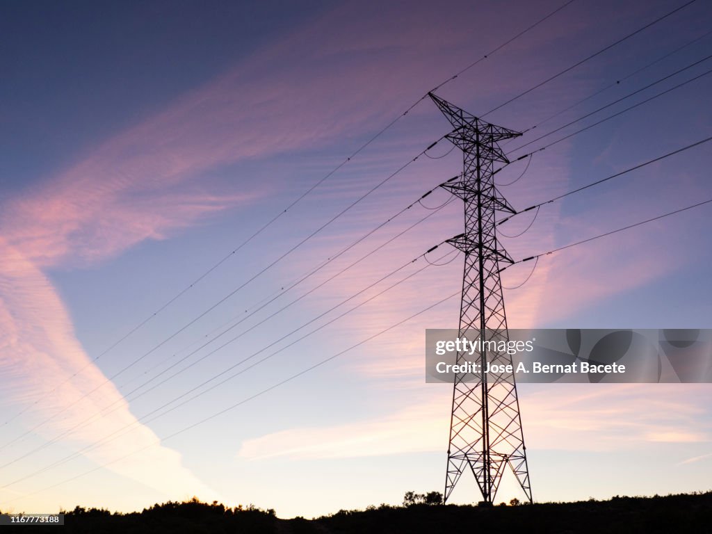 Big electrical towers of high tension for the distribution of electricity in a sunset in the mountain.