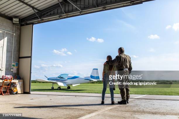 rear view of daughter and father looking at view from airplane hangar - airplane hangar stock pictures, royalty-free photos & images