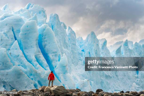 man with red jacket standing in front of the snout of perito moreno glacier, el calafate, santa cruz province, argentina. - el calafate stockfoto's en -beelden