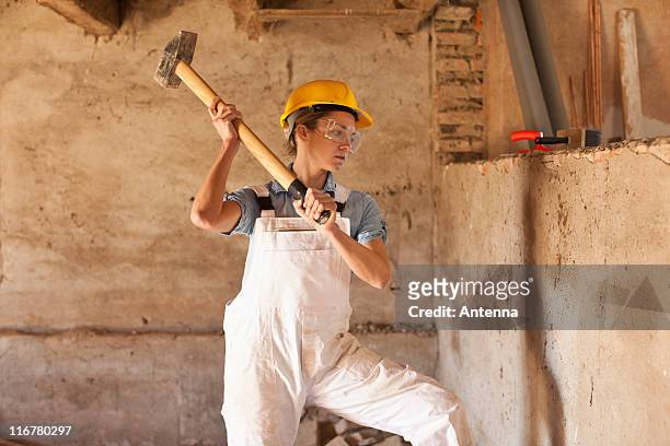 a female construction worker swinging a sledgehammer - sledgehammer stock-fotos und bilder