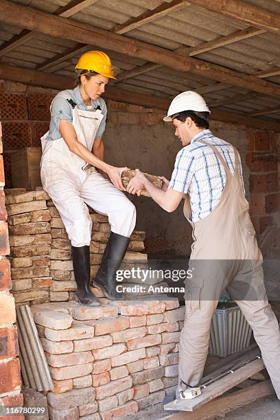 manual workers moving bricks at a building site - female bricklayer stock pictures, royalty-free photos & images