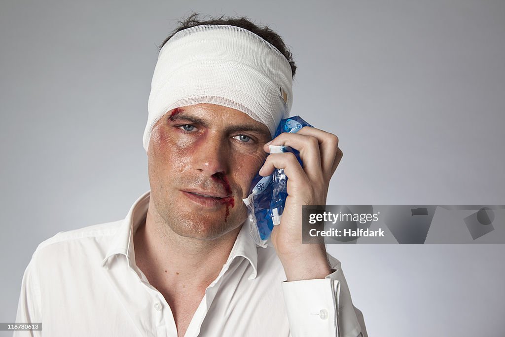 A man with bruises and a bandaged head holding an ice pack to his face