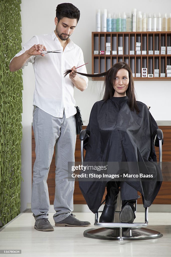 A woman having her hair cut by a male hairdresser