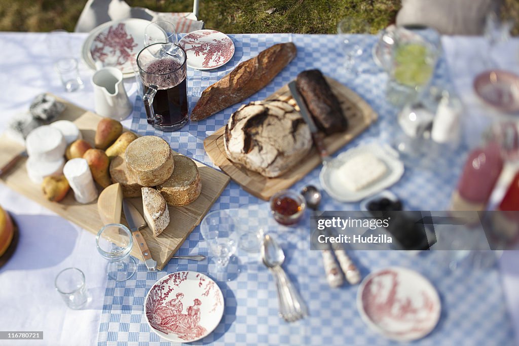 Cheese wheels, bread and a lot of crockery on a dining table outside