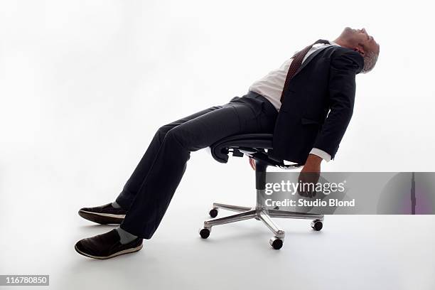 an exhausted businessman sleeping in an office chair - recostarse fotografías e imágenes de stock