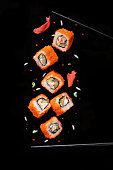 Sushi pieces between chopsticks, flying separated on black background.