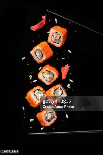 sushi pieces between chopsticks, flying separated on black background. - food mid air stock pictures, royalty-free photos & images