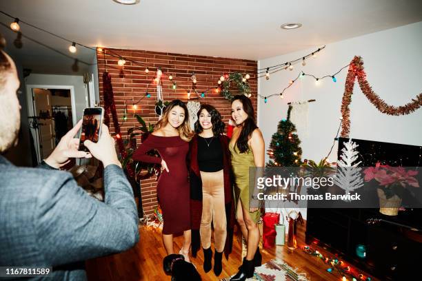 man taking photo with smart phone of smiling female friends during holiday party in home - four people stock pictures, royalty-free photos & images