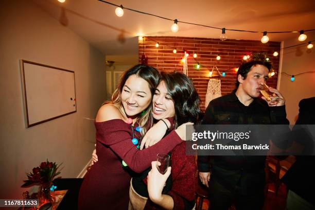 smiling female friends hugging during holiday party in home - casa navidad fotografías e imágenes de stock