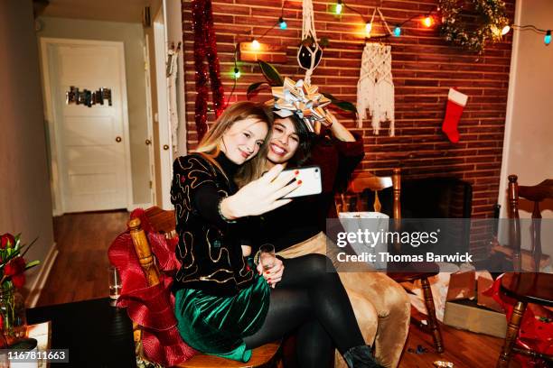 smiling female friends posing for selfie with bow over their heads during holiday party in home - christmas cool attitude stock pictures, royalty-free photos & images