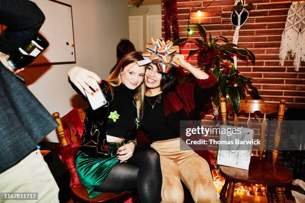 smiling female friends posing for selfie with bow over their heads during holiday party in home - christmas selfie stock pictures, royalty-free photos & images