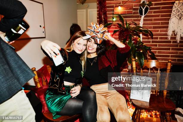 smiling female friends posing for selfie with bow over their heads during holiday party in home - christmas interior stock pictures, royalty-free photos & images