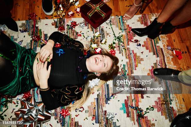 laughing woman lying on floor covered in bows and confetti during holiday party with friends - christmas gift stock pictures, royalty-free photos & images