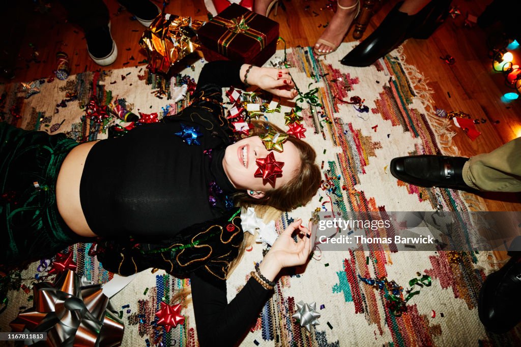 Laughing woman lying on floor with bows over eyes during holiday party with friends