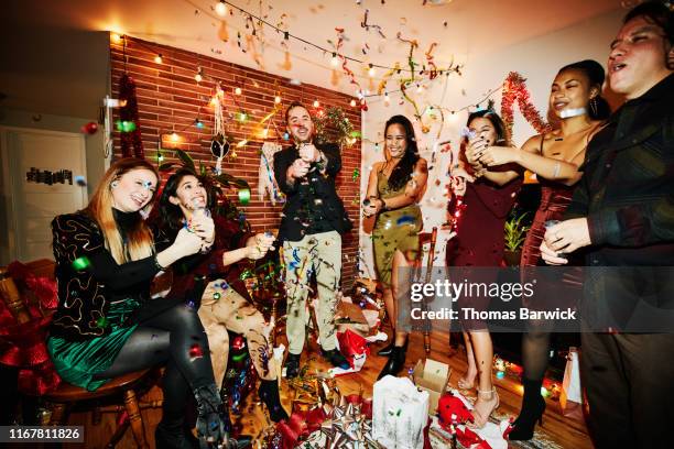 smiling and laughing friends shooting party poppers during holiday party in home - christmas party dress stockfoto's en -beelden