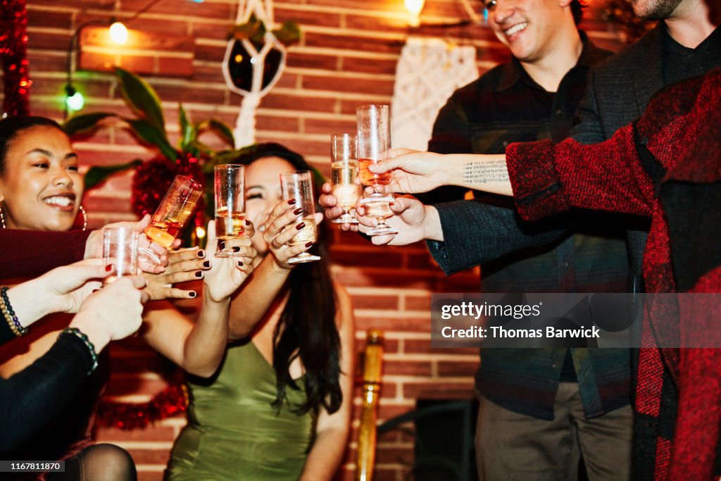 Smiling friends toasting with champagne glasses during holiday party in home