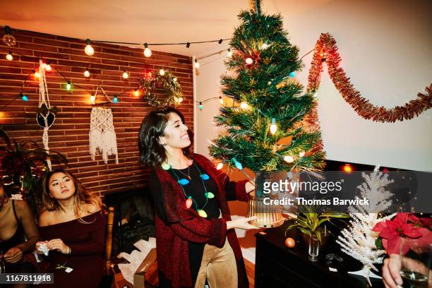 Smiling woman holding miniature Christmas tree during holiday party with friends