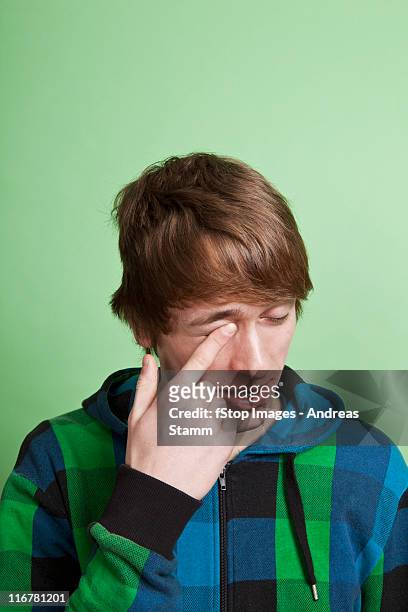 a teenage boy rubbing his eye with his finger, portrait, studio shot - rubbing eyes stockfoto's en -beelden