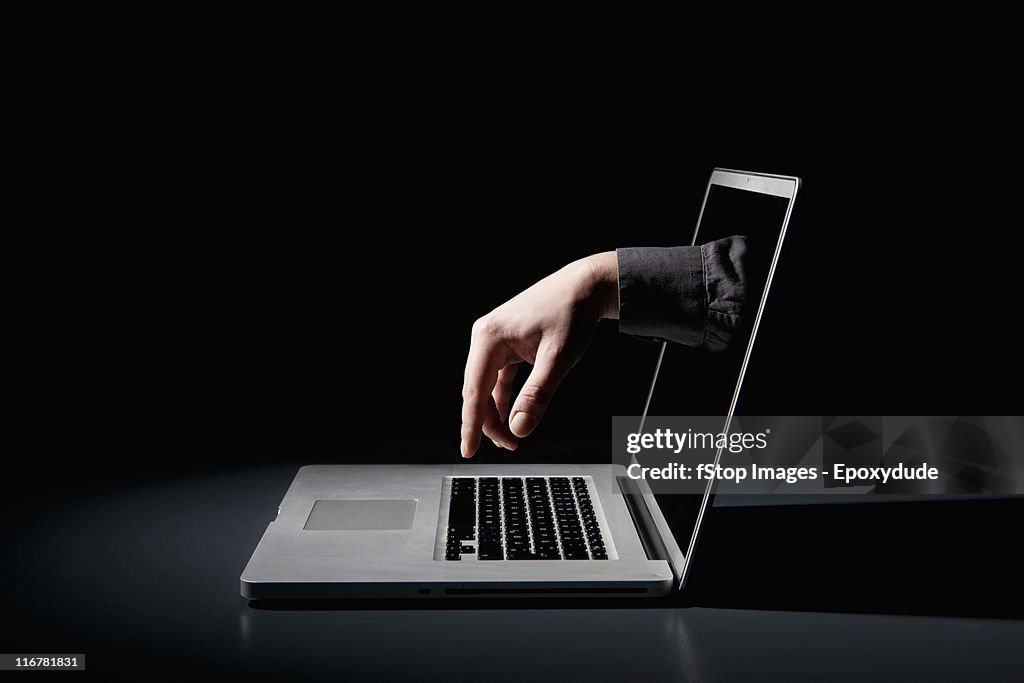 A hand reaching through a laptop to type on the keyboard