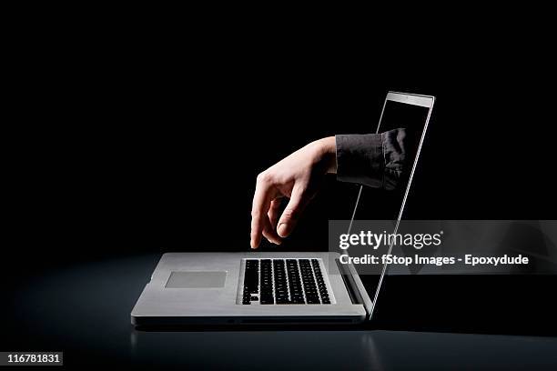 a hand reaching through a laptop to type on the keyboard - appearance stock-fotos und bilder