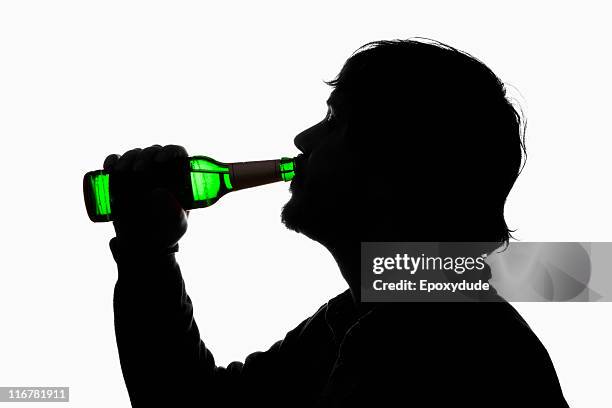 a silhouetted man drinking beer from a bottle - alcoholic stock pictures, royalty-free photos & images