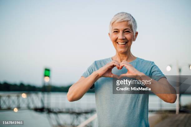 femme aîné actif faisant un coeur avec ses mains - happy people running photos et images de collection