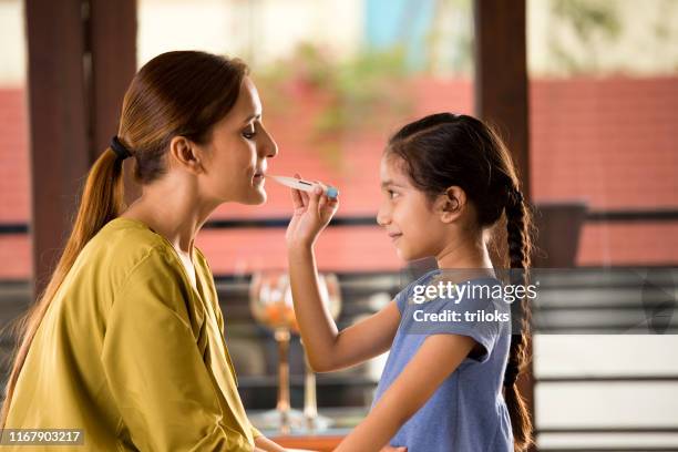 girl examining her mother using thermometer - indian mother and child stock pictures, royalty-free photos & images